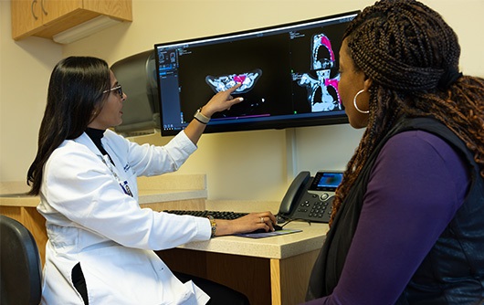 Doctor Arpi Thukral points to a scan of a breast tumor on a screen while talking to a female patient.