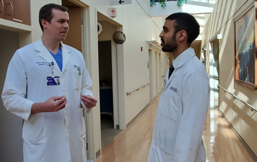 Two Proton Center physicians talking to each other in a hallway wearing white lab coats.