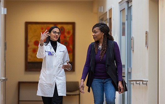 Doctor Arpi Thukral walking down the hall next to a young African American woman who is listening to her speak.