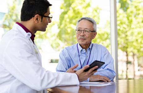 A male proton therapy physician and elderly male patient discussing a scan.