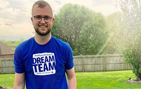 A young man who completed proton therapy smiling at the camera while walking in his yard.