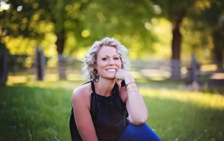 Sherri Kalmer smiling at the camera while sitting in a green field.