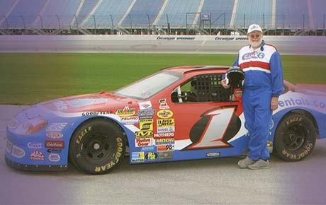 A man holding a helmet while standing next to his race car.