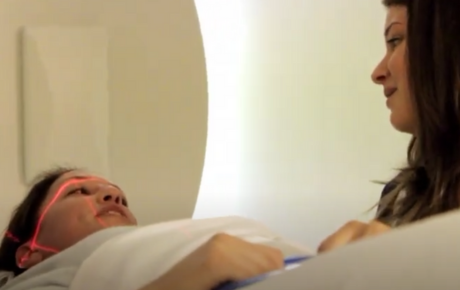 A woman preparing to have a brain scan who is looking at a nurse with long brown hair.