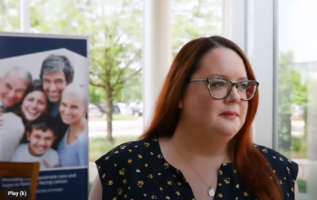 Proton Center patient Katie E. looking out a window in front of a banner with smiling faces on it.