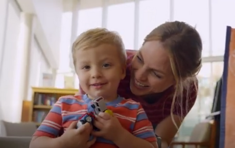 A child name Luke wearing a bright striped shirt being hugged by his mom from behind.