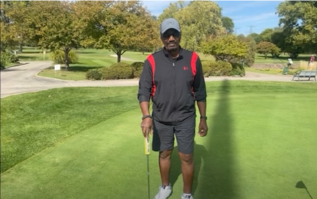 Proton Center patient Sidney standing on a green golf course holding a golf club on a sunny day.