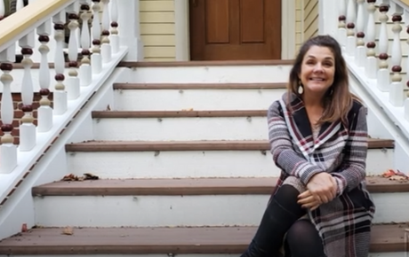 Proton Center patient Wendy sitting on the steps of a house and smiling with her arms crossed over her legs.